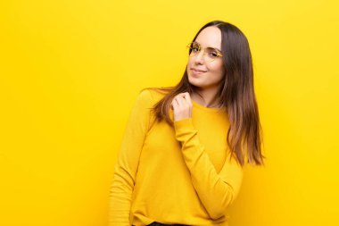 Genç, güzel bir kadın kibirli, başarılı, pozitif ve gururlu görünüyor. Turuncu duvara karşı kendini gösteriyor.