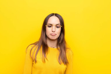 Genç ve güzel bir kadın aptal ve komik görünüyor. Aptal şaşı bir ifadeyle, şakalaşıyor ve turuncu duvarda oynaşıyor.