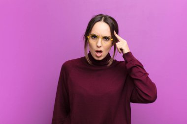 Genç, güzel bir kadın şaşırmış, ağzı açık, şok olmuş, mor duvara karşı yeni bir düşünce, fikir ya da konsept keşfediyor.