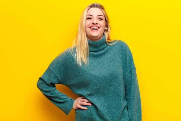 若いかなりブロンドの女性は喜んで手で笑顔でヒップと自信を持って 誇りと黄色の壁に対する友好的な態度 — ストック写真