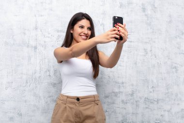 Genç ve güzel bir kadın akıllı telefonu grunge duvarına karşı kullanıyor.