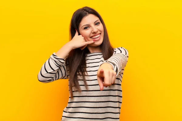 若い可愛い女性がカメラを指差しながら笑顔で後でジェスチャーをして黄色の壁に電話で話します — ストック写真