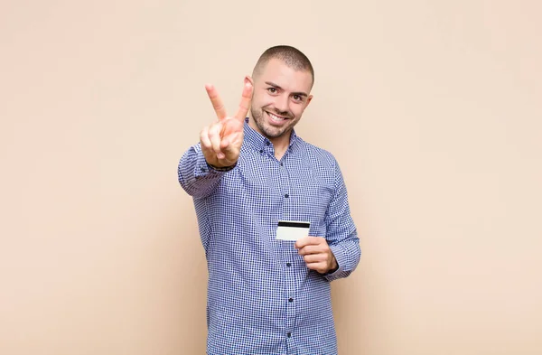 笑顔で幸せそうで気楽でポジティブな若いハンサムな男クレジットカードで片手で勝利や平和をジェスチャー — ストック写真