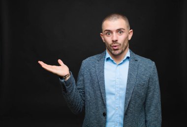 Genç işadamı şaşırmış ve şok olmuş görünüyor, çenesi düşmüş ve düz duvara karşı eli açık bir obje tutuyor.