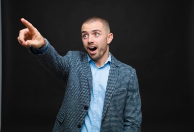 Genç işadamı şok olmuş ve şaşırmış hissediyor, şaşkınlıkla yukarı bakıyor, şaşırmış, ağzı açık bir şekilde düz duvara bakıyor.