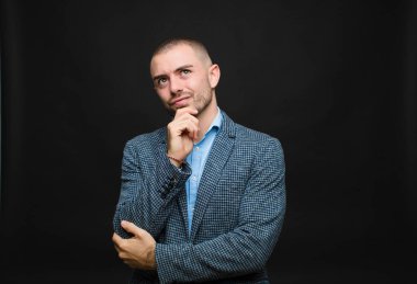 Genç işadamı düşünüyor, şüpheci ve şaşkın hissediyor, farklı seçenekleri var, düz duvara karşı hangi kararı vereceğimi merak ediyor.