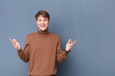 Genç sarışın adam kendini mutlu, şaşkın, şanslı ve şaşırmış hissediyor. Düz duvara yaslandığına inanamıyorum.