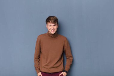 Genç, sarışın bir adam neşeli ve tesadüfen gülümsüyor. Olumlu, mutlu, kendine güvenen ve rahat bir yüz ifadesi var. Duvara yaslanmış.