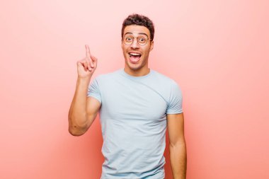 Genç Arap bir adam bir fikri fark ettikten sonra mutlu ve heyecanlı bir dahi gibi hissediyor, neşeli bir şekilde parmağını kaldırıyor, eureka! Pembe duvara yaslan