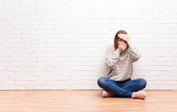 young blonde pretty girl covering face with both hands saying no to the camera! refusing pictures or forbidding photos sitting on the floor