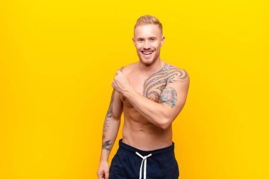 Genç güçlü sarışın adam mutlu, pozitif ve başarılı hissediyor, meydan okumayla karşılaştığında motive oluyor veya sarı duvara karşı iyi sonuçları kutluyor.