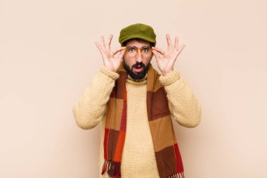 Genç havalı sakallı adam şok olmuş, şaşırmış ve şaşırmış hissediyor, elinde şaşkın, inançsız bir bakışla gözlük tutuyor.