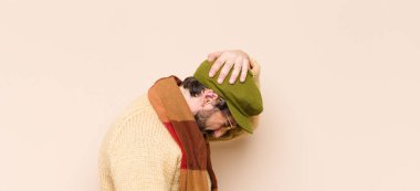 Havalı sakallı genç adam stresli ve hayal kırıklığına uğramış hissediyor, el ele tutuşuyor, yorgun, mutsuz ve migren ağrısı çekiyor.