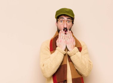 Genç havalı sakallı adam şok olmuş, şaşırmış bir ifadeyle ağzını kapatıyor, sır saklıyor ya da 