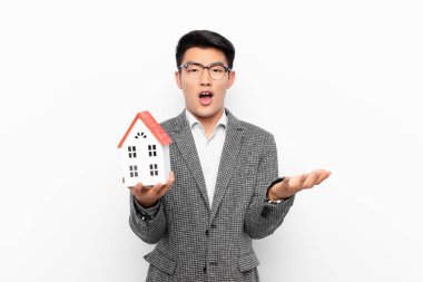 Genç Japon bir adam şok olmuş ve şaşırmış, endişeli ve paniklemiş hissediyor. Stresli ve dehşete düşmüş bir şekilde ev modelini izliyor.
