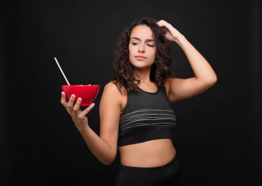 Genç, güzel bir kadın şaşkın ve kafası karışmış hissediyor. Kafasını kaşıyor ve yanına bakıyor. Sağlıklı bir kâse yiyor.