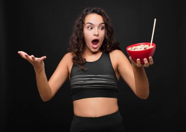 Genç ve güzel bir kadın şok olmuş ve şaşırmış, endişeli ve panik içinde, stresli ve dehşete düşmüş bir şekilde kahvaltıda sağlıklı bir kase yiyor.