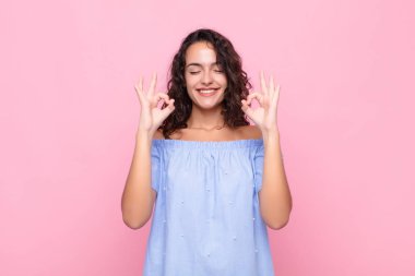 Genç ve güzel bir kadın konsantre olmuş ve meditasyon yapıyor. Tatmin olmuş ve rahatlamış hissediyor. Pembe duvara karşı bir seçim yapıyor.