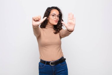 Genç, güzel bir kadın gülümsüyor ve arkadaş canlısı görünüyor. Altı ya da altıncı numarayı gösteriyor. Elleri önde, beyaz duvara doğru sayıyor.