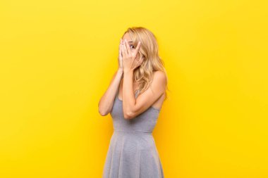 Genç sarışın kadın korkmuş ya da utanmış hissediyor. Gözleri turuncu duvara dönük bir şekilde dikizliyor ya da dikizliyor.