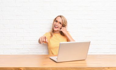 Genç sarışın kadın neşeli bir şekilde gülümsüyor ve kamerayı işaret ediyor. Daha sonra seni arıyor, telefonda dizüstü bilgisayarla konuşuyor.