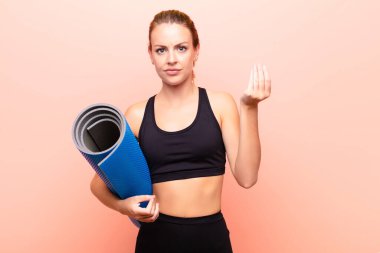 Kızıl saçlı güzel kadın kapiş ya da para hareketi yapıyor, sana borçlarını ödemeni söylüyor! Elinde yoga minderi var..