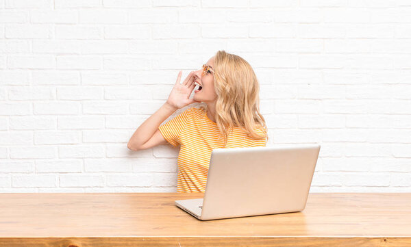 young blonde woman profile view, looking happy and excited, shouting and calling to copy space on the side using a laptop
