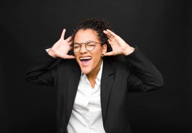 Genç siyahi kadın panik ya da öfke içinde bağırıyor, şok olmuş, korkmuş ya da öfkeli, elleri başının yanında siyah duvara yaslanmış.