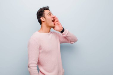 Genç Arap adam profil görüntüsü, mutlu ve heyecanlı görünüyor, bağırıyor ve gri duvara karşı alan kopyalamak için çağırıyor