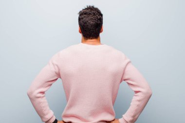 Genç Arap adam kafası karışık ya da dolu hissediyor ya da şüphe ve sorular, merak ediyor, elleri kalçasında, gri duvara karşı dikiz görüşlü