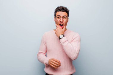 Ağzı ve gözleri sonuna kadar açık, eli çenesinde olan genç bir Arap adam, hoş olmayan bir şok geçiriyor, gri duvara karşı ne söylüyor ya da vay be diyor.