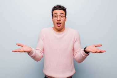 Genç Arap adam son derece şaşırmış, şaşırmış, endişeli ve paniklemiş, stresli ve dehşete kapılmış bir şekilde gri duvara bakıyor.