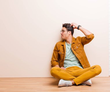 Genç Arap bir adam bilgisiz ve kafası karışık, bir çözüm düşünüyor, eli kalçasında, diğeri kafasında, dikiz aynası yerde oturuyor.