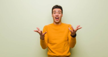 Genç Arap adam ağzı açık ve şaşkın, şaşırmış ve şaşırmış düz duvara karşı inanılmaz bir sürprizle