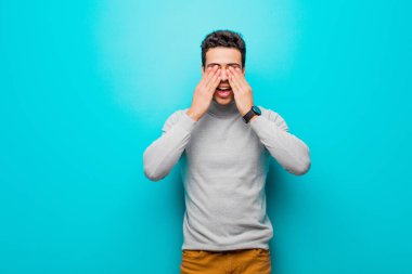 Genç Arap adam gülümsüyor ve mutlu hissediyor, iki eliyle gözlerini kapatıyor ve düz duvara karşı inanılmaz bir sürpriz bekliyor.