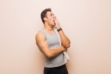 Genç Arap adam sabahın erken saatlerinde uykulu, yorgun ve sıkılmış olarak uyanıyor ve esniyor. spor konsepti