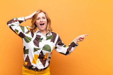 Orta yaşlı bir kadın gülüyor, mutlu, pozitif ve şaşırmış görünüyor, yanal fotokopi alanını işaret eden harika bir fikrin farkına varıyor.