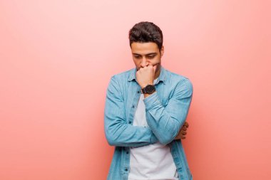 Genç Arap adam ciddi, düşünceli ve endişeli, elleri pembe duvara yaslanmış bir şekilde yan bakıyor.