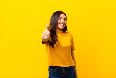 Genç Latin güzel kadın gururlu, kaygısız, kendinden emin ve mutlu, parmakları düz duvara değmiş bir şekilde gülümsüyor.