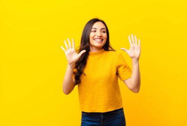 Genç Latin güzel bayan gülümsüyor ve arkadaş canlısı görünüyor, onuncu ya da onuncu numarayı gösteriyor, eli önde, düz duvara doğru sayıyor.