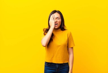 Genç Latin güzel bir kadın uykulu görünüyor, sıkılmış ve esniyor, baş ağrısı ve bir eliyle yüzünün yarısını düz duvara yapıştırıyor.