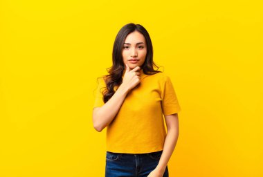 Genç Latin güzel kadın ciddi görünüyor, kafası karışık, kararsız ve düşünceli, seçenekler veya düz duvara karşı seçimler arasında şüpheci