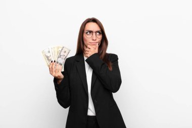 Genç iş kadını düşünüyor, kuşkulu ve şaşkın hissediyor, farklı seçeneklerle, dolar banknotlarıyla hangi kararı vereceğini merak ediyor.