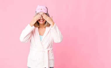 Orta yaşlı bir kadın gülümsüyor ve mutlu hissediyor, iki eliyle gözlerini kapatıyor ve inanılmaz bir sürpriz bekliyor. gece elbisesi konsepti