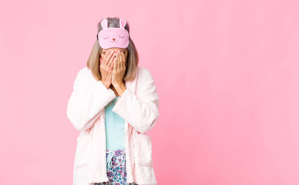 middle age woman feeling sad, frustrated, nervous and depressed, covering face with both hands, crying. night suit concept