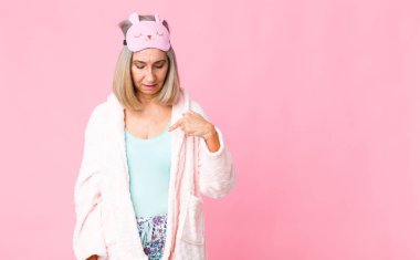 Orta yaşlı bir kadın neşeyle gülümsüyor, yere bakıyor ve göğsüne işaret ediyor. gece elbisesi konsepti