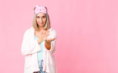 Orta yaşlı bir kadın mutlu ve aşık, bir eli kalbinin yanında, diğer eli önde uzanmış şekilde gülümsüyor. gece elbisesi konsepti