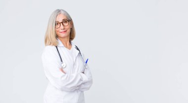 Orta yaşlı doktor kadın kameraya çapraz kollarıyla gülümsüyor ve mutlu, kendinden emin, tatmin olmuş bir yüz ifadesi var.