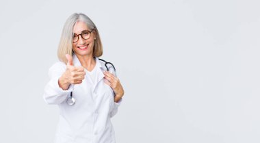 Orta yaşlı doktor kadın gururlu, tasasız, kendinden emin ve mutlu, başparmağıyla olumlu gülümsüyor.