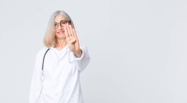 Orta yaşlı doktor kadın gülümsüyor ve arkadaş canlısı görünüyor, 4 ya da 4 numarayı gösteriyor, eli önde, geri sayıyor.